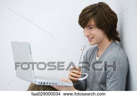 Young man looking at laptop computer, speaking into microphone, side view View Large Photo Image Picture - Young man looking at laptop computer, speaking into microphone, side view. Fotosearch