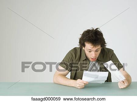 Young man looking at letter, reacting with surprise View Large Photo Image Stock Photo - Young man looking at letter, reacting with surprise. Fotosearch
