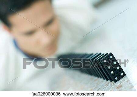 Young man looking at row of dominoes, focus on foreground View Large Photo Image Stock Photograph - Young man looking at row of dominoes, focus on foreground. Fotosearch