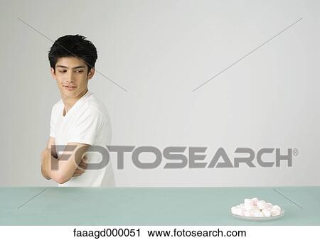 Young man looking over shoulder at plate of marshmallows View Large Photo Image Stock Image - Young man looking over shoulder at plate of marshmallows. Fotosearch