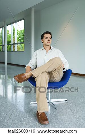 Young man sitting in chair, full length View Large Photo Image Stock Photograph - Young man sitting in chair, full length. Fotosearch
