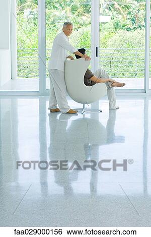 Young man sitting in chair next to window, father standing behind, smiling over shoulder at camera View Large Photo Image Stock Photograph - Young man sitting in chair next to window, father standing behind, smiling over shoulder at camera. Fotosearch