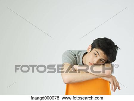 Stock Photo - Young man sitting, leaning head on back of chair. Fotosearch