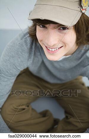 Young man sitting on the ground, smiling at camera, high angle view View Large Photo Image Picture - Young man sitting on the ground, smiling at camera, high angle view. Fotosearch