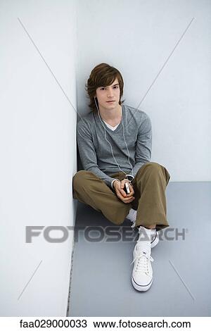 Young man sitting on the ground, listening to MP3 player, looking at camera View Large Photo Image Stock Image - Young man sitting on the ground, listening to MP3 player, looking at camera. Fotosearch