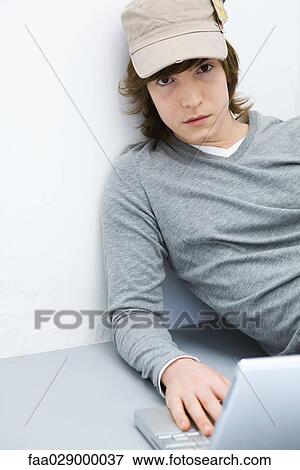 Young man sitting on the ground, using laptop computer, looking at camera View Large Photo Image Stock Photo - Young man sitting on the ground, using laptop computer, looking at camera. Fotosearch