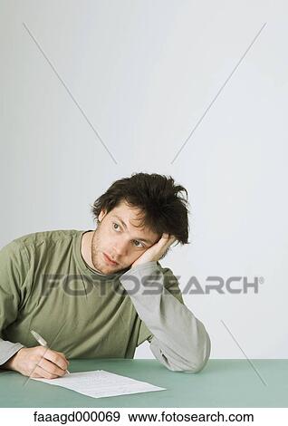 Stock Photo - Young man writing, leaning on elbow and looking away. Fotosearch