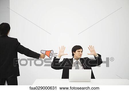 Young professional sitting in front of laptop computer with hands raised, colleague aiming megaphone at him View Large Photo Image Stock Image - Young professional sitting in front of laptop computer with hands raised, colleague aiming megaphone at him. Fotosearch