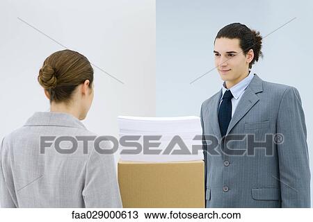 Young professionals standing face to face, documents stacked on cardboard box between them View Large Photo Image Stock Image - Young professionals standing face to face, documents stacked on cardboard box between them. Fotosearch