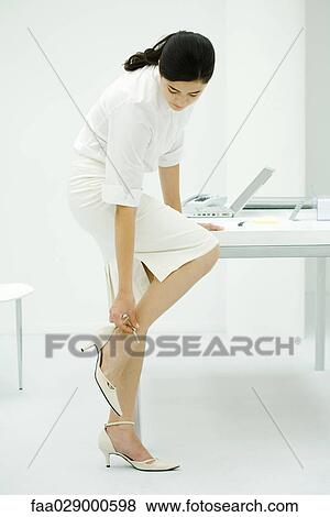 Young woman bending over to adjust strap of high heel shoe, full length View Large Photo Image Stock Photo - Young woman bending over to adjust strap of high heel shoe, full length. Fotosearch
