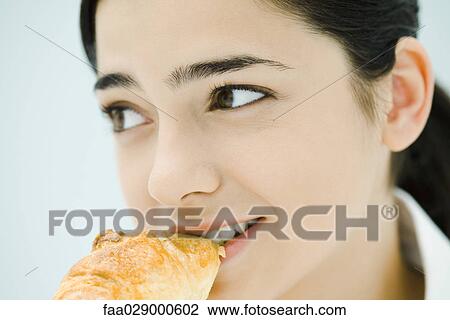 Stock Image - Young woman eating croissant, close-up. Fotosearch
