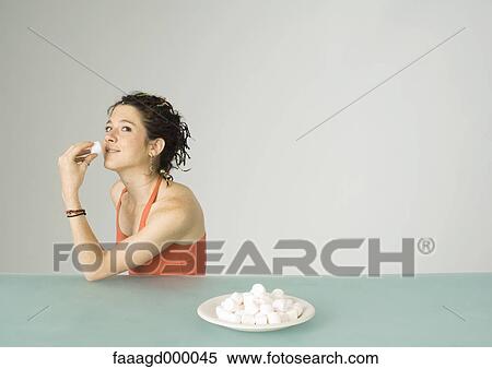 Stock Photography - Young woman eating marshmallows. Fotosearch