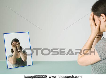 Stock Photo - Young woman facing mirror with hands over face. Fotosearch