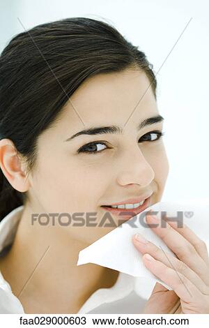 Stock Image - Young woman holding napkin against mouth, smiling at camera. Fotosearch