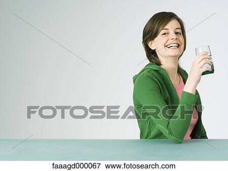 Stock Photo - Young woman holding up glass, smiling. Fotosearch