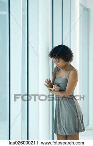 Young woman leaning against pole, looking down at cell phone View Large Photo Image Stock Image - Young woman leaning against pole, looking down at cell phone. Fotosearch