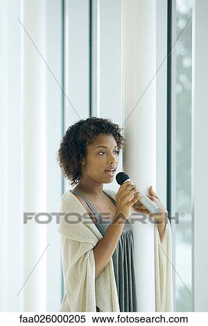 Young woman leaning against pole, singing into microphone, looking away View Large Photo Image Stock Photography - Young woman leaning against pole, singing into microphone, looking away. Fotosearch