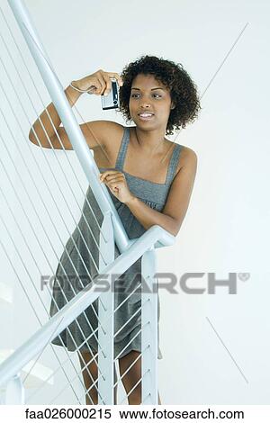 Young woman leaning against railing, holding up digital camera View Large Photo Image Stock Photography - Young woman leaning against railing, holding up digital camera. Fotosearch