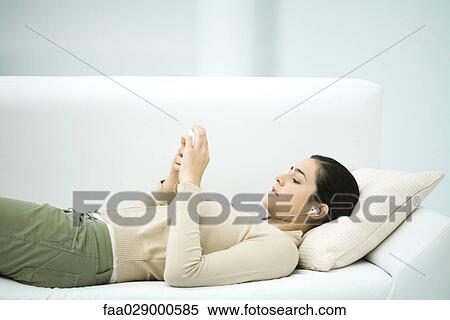 Stock Photography - Young woman lying on couch, listening to MP3 player. Fotosearch