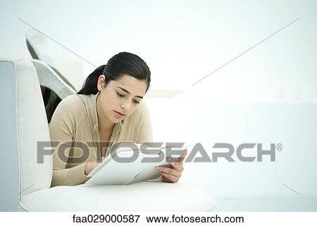 Stock Photo - Young woman lying on couch, reading book. Fotosearch