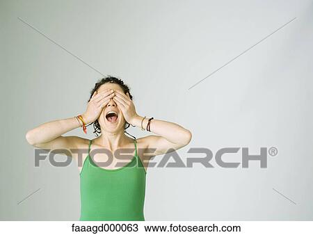 Stock Image - Young woman screaming and covering eyes. Fotosearch