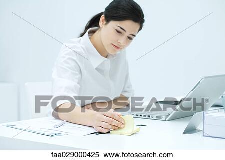 Young woman sitting at desk, flipping through adhesive note block View Large Photo Image Stock Photography - Young woman sitting at desk, flipping through adhesive note block. Fotosearch