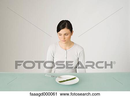 Young woman sitting in front of plate with single asparagus, looking away View Large Photo Image Stock Image - Young woman sitting in front of plate with single asparagus, looking away. Fotosearch