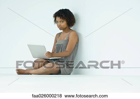 Stock Photo - Young woman sitting on the ground, using laptop computer, smiling at camera. Fotosearch