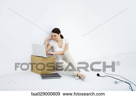 Young woman sitting on the ground, using laptop computer, loose electric cords nearby View Large Photo Image Stock Photo - Young woman sitting on the ground, using laptop computer, loose electric cords nearby. Fotosearch