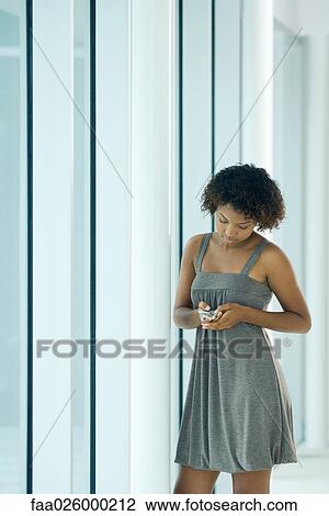 Young woman standing next to pole, looking down at cell phone View Large Photo Image Stock Image - Young woman standing next to pole, looking down at cell phone. Fotosearch