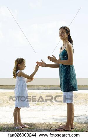 Young woman standing outdoors, playing clapping game with little sister, smiling at camera View Large Photo Image Picture - Young woman standing outdoors, playing clapping game with little sister, smiling at camera. Fotosearch
