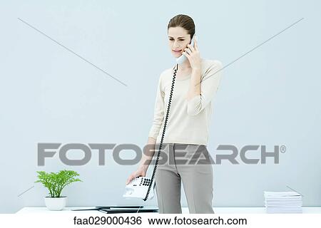 Stock Photograph - Young woman standing, using phone. Fotosearch