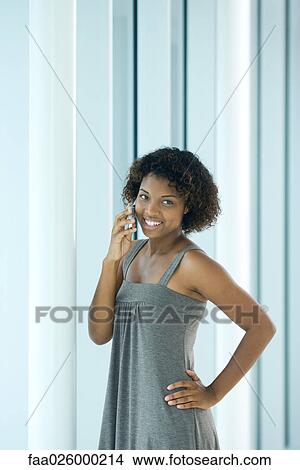 Young woman standing with hand on hip, using cell phone, smiling View Large Photo Image Picture - Young woman standing with hand on hip, using cell phone, smiling. Fotosearch