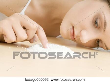 Stock Image - Young woman touching pile of powder on table. Fotosearch