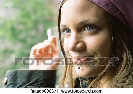 Stock Image - Young woman with facial piercing, smoking, close-up. Fotosearch