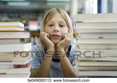 Boy leaning on elbow with look of boredom, stacks of books in foreground View Large Photo Image Stock Image - Boy leaning on elbow with look of boredom, stacks of books in foreground. Fotosearch