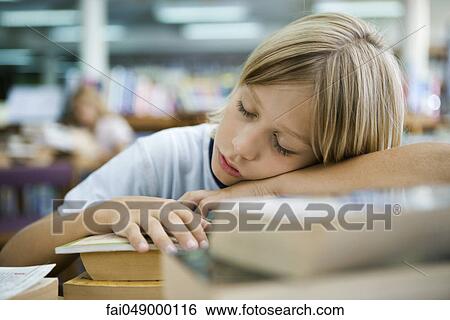 Stock Photograph - Boy napping with head resting on arms in library. Fotosearch