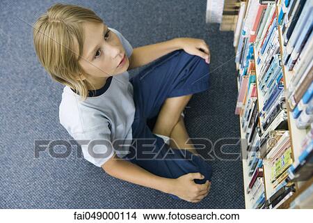 Boy sitting on floor looking up at rows of books lining bookcase View Large Photo Image Picture - Boy sitting on floor looking up at rows of books lining bookcase. Fotosearch