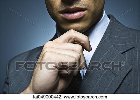 Stock Image - Businessman with hand under chin, cropped portrait. Fotosearch