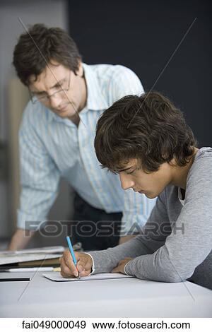 Stock Photo - College student working on assignment, teacher assisting. Fotosearch
