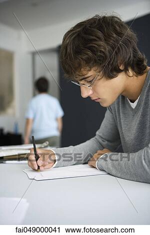 Stock Image - College student writing at desk in classroom. Fotosearch