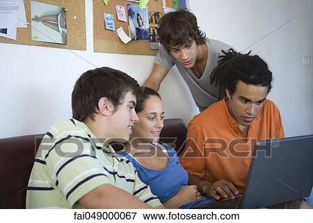 Stock Photo - College students gathered around classmate using laptop computer. Fotosearch