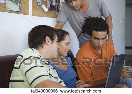 Stock Photograph - College students gathered around classmate using laptop computer. Fotosearch