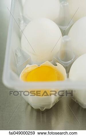 Stock Photo - Eggs in carton, one cracked open. Fotosearch