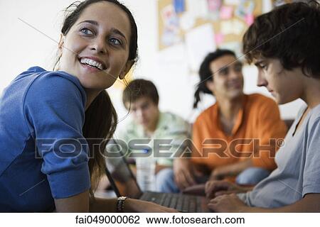 Female college student smiling, looking over shoulder, sitting next to friend using laptop computer View Large Photo Image Stock Image - Female college student smiling, looking over shoulder, sitting next to friend using laptop computer. Fotosearch