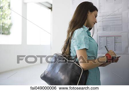 Female college student standing at bulletin board writing in agenda View Large Photo Image Stock Photograph - Female college student standing at bulletin board writing in agenda. Fotosearch