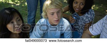 Group of young adult friends sitting on grass, one young woman holding drink can View Large Photo Image Stock Image - Group of young adult friends sitting on grass, one young woman holding drink can. Fotosearch