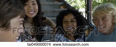 Group of young adult friends sitting outdoors, chatting and smiling View Large Photo Image Picture - Group of young adult friends sitting outdoors, chatting and smiling. Fotosearch
