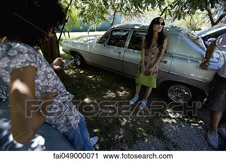 Stock Image - Group of young friends meeting at park, standing in shade leaning against cars. Fotosearch