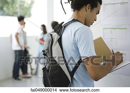 Male college student at bulletin board writing notes in notebook View Large Photo Image Picture - Male college student at bulletin board writing notes in notebook. Fotosearch